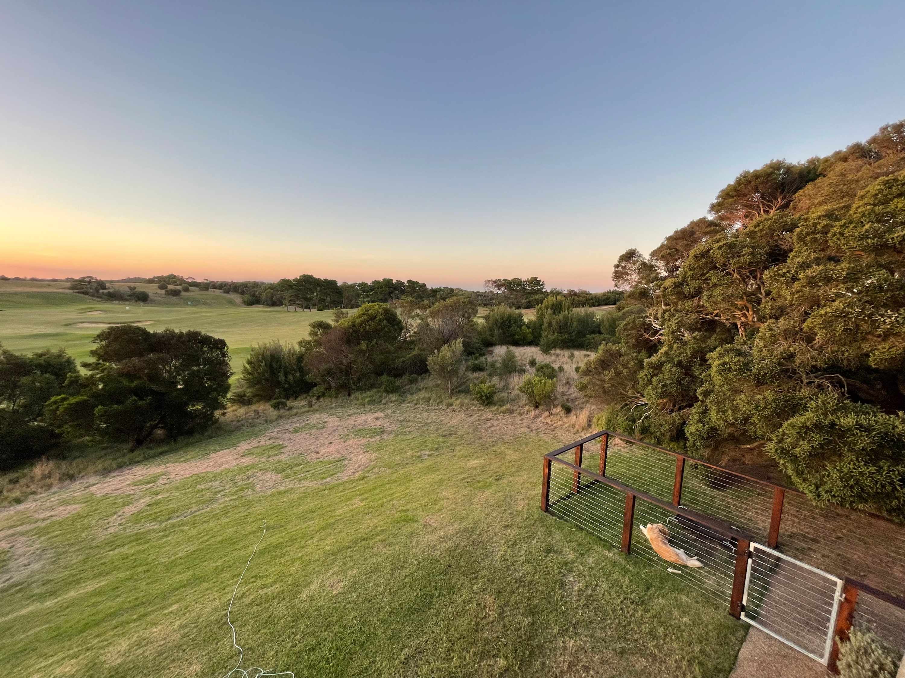 Dusk over a green valley edged with coastal scrub, the sky fading from blue to orange