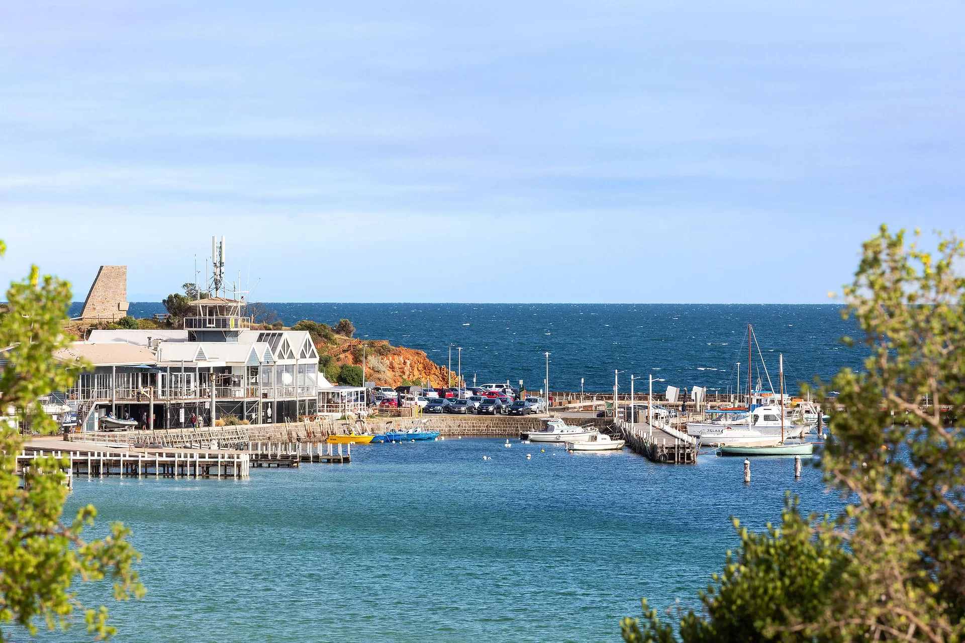 Mornington's harbour on a clear day, with a waterfront building, moored boats and the red cliffs of Schnapper Point