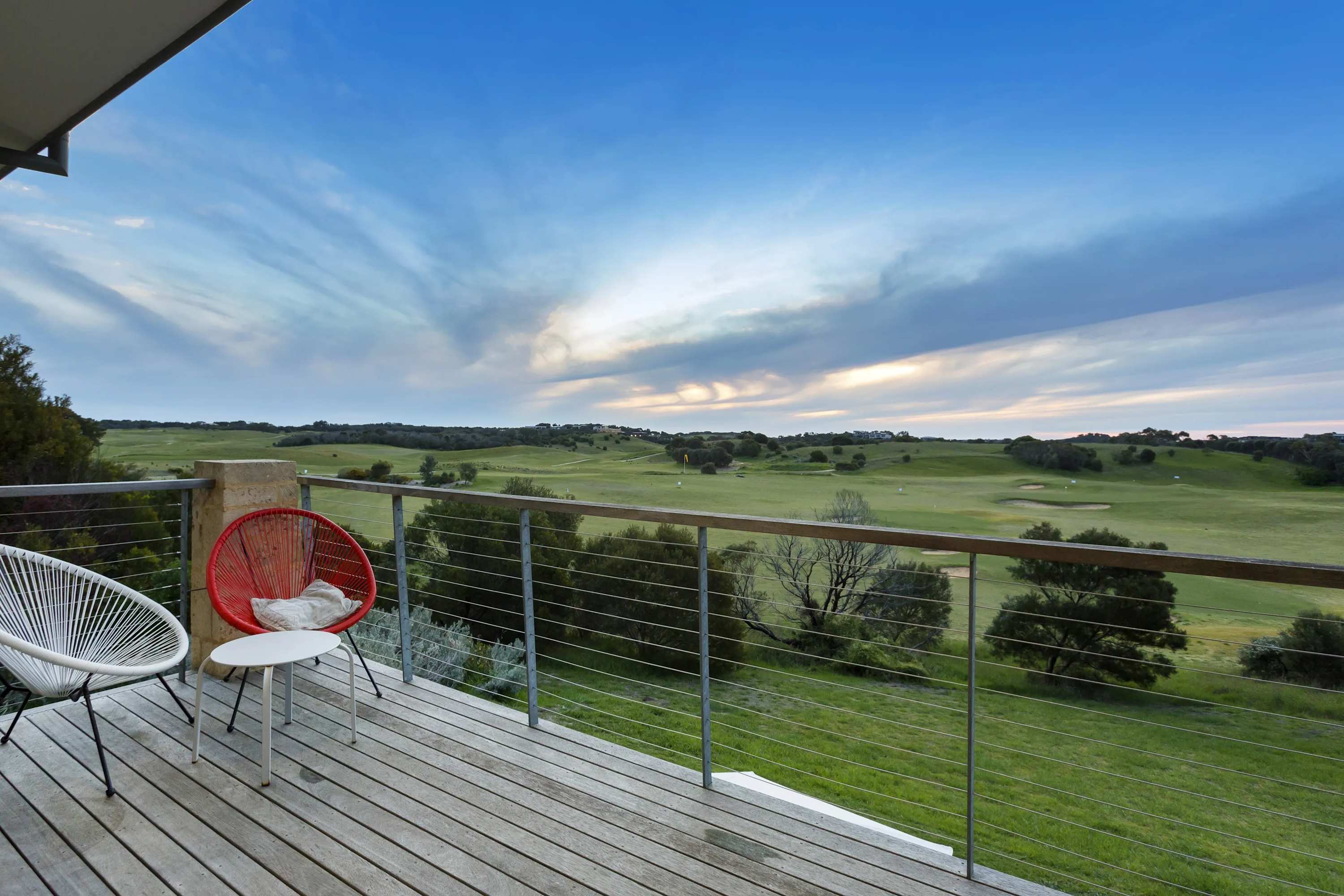 Two chairs on a deck looking out over rolling green fairways and coastal scrub under a wide sky
